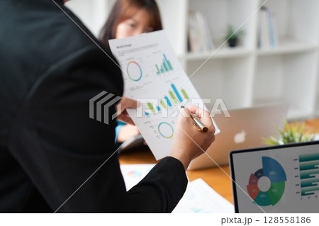 Business Meeting with Colleagues Analyzing Financial Reports and Graphs in a Modern Office Setting Business Meeting with Colleagues Analyzing Financial Reports and Graphs in a Modern Office Setting 128558186