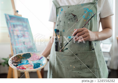 Artist Holding Paintbrush and Palette in Studio with Canvas in Background 128558282