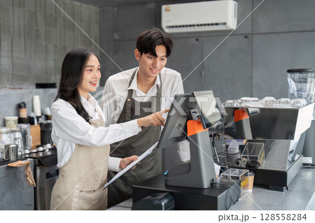 Young Baristas Working Together at a Modern Coffee Shop Counter with a Touchscreen Register Young Baristas Working Together at a Modern Coffee Shop Counter with a Touchscreen Register 128558284