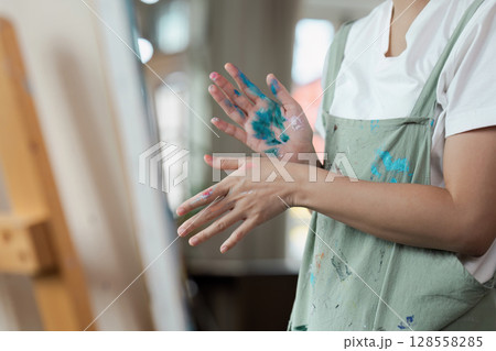 Artist with Paint-Splattered Hands in Apron Creating Art in Studio Artist with Paint-Splattered Hands in Apron Creating Art in Studio 128558285