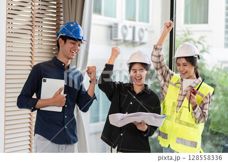 Group of Happy Engineers Celebrating Success at Construction Site with Blueprints and Safety Gear Group of Happy Engineers Celebrating Success at Construction Site with Blueprints and Safety Gear 128558336