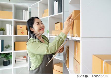 Smiling Small Business Owner Organizing Inventory on Shelves in Modern Office Space Smiling Small Business Owner Organizing Inventory on Shelves in Modern Office Space 128558350
