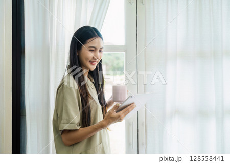 Young Woman Using Tablet and Drinking Coffee in the morning - Modern Technology and Lifestyle Concept 128558441