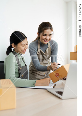 Two Female Entrepreneurs Working Together in a Small Business Office, Packaging Products for Online Orders 128558523
