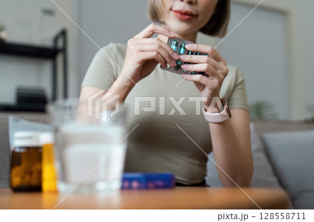 Woman Organizing Medication at Home with Pill Organizer and Glass of Water on Table 128558711