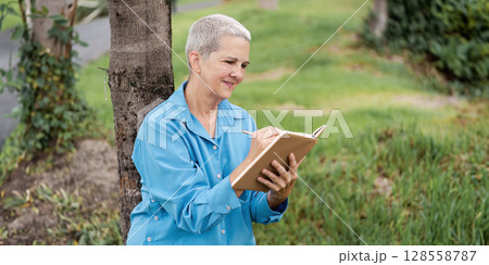 Senior Woman Reading a Book Outdoors in a Park on a Sunny Day 128558787