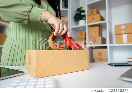 Small Business Owner Packing Orders in Home Office with Cardboard Boxes and Shipping Supplies Small Business Owner Packing Orders in Home Office with Cardboard Boxes and Shipping Supplies 128558872