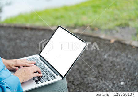 Person Typing on Laptop with Blank Screen Outdoors on a Gravel Path with Green Grass Background Person Typing on Laptop with Blank Screen Outdoors on a Gravel Path with Green Grass Background 128559137