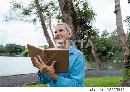 Senior Woman Reading a Book in a Park by a Lake on a Cloudy Day Senior Woman Reading a Book in a Park by a Lake on a Cloudy Day 128559154