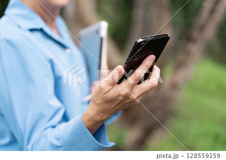 Business Professional Using Smartphone and Tablet Outdoors in a Natural Setting 128559159