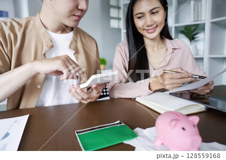 Young Couple Calculating Savings with Calculator and Documents at Home, Planning Financial Future Together Young Couple Calculating Savings with Calculator and Documents at Home, Planning Financial Future Together 128559168