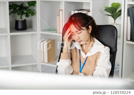 Young Office Worker Experiencing Headache Due to Office Syndrome in Modern Workspace with Shelves and Plants 128559224