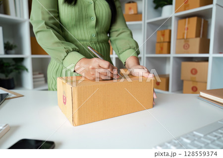 Small Business Owner Preparing Package for Shipment in Modern Office Space with Shelves of Boxes Small Business Owner Preparing Package for Shipment in Modern Office Space with Shelves of Boxes 128559374