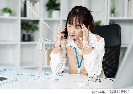 Stressed Businesswoman on Phone Call in Modern Office with Documents and Charts on Desk 128559464