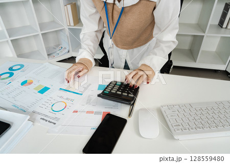 Businesswoman Analyzing Financial Reports with Calculator at Modern Office Desk Businesswoman Analyzing Financial Reports with Calculator at Modern Office Desk 128559480
