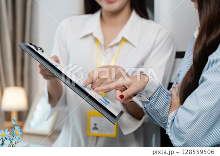 Professional Businesswomen Collaborating on Project with Clipboard in Modern Office Setting Professional Businesswomen Collaborating on Project with Clipboard in Modern Office Setting 128559506