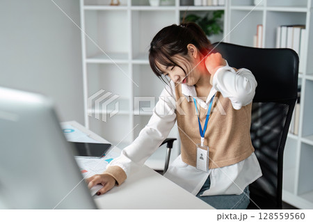 Young Woman Experiencing Neck Pain While Working at Desk in Modern Office Environment 128559560
