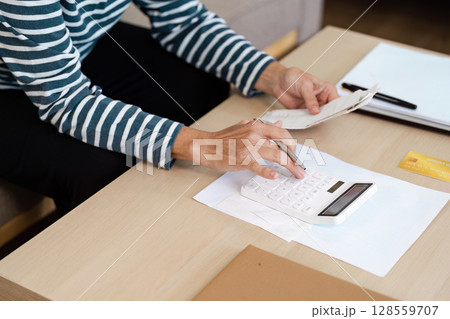 Senior Calculating financial at Home with Calculator and Receipt on Wooden Table, Managing Personal Budget Senior Calculating financial at Home with Calculator and Receipt on Wooden Table, Managing Personal Budget 128559707