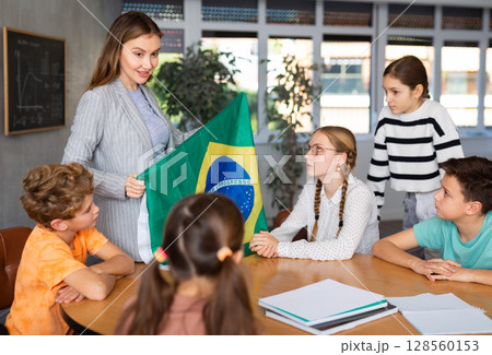 Teacher holds the flag of Brazil in her hands and tells the students about country Teacher holds the flag of Brazil in her hands and tells the students about country 128560153