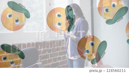 Multiple sick face emojis moving against woman wearing face mask talking on smartphone at office 128560211