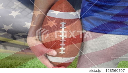 Waving american flag over mid section of male rugby player holding a ball against sports stadium 128560507