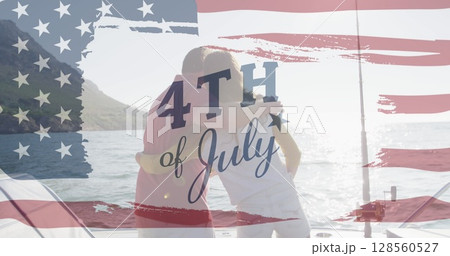 Image of text july 4th with american flag billowing over back view of couple embracing by sea Image of text july 4th with american flag billowing over back view of couple embracing by sea 128560527