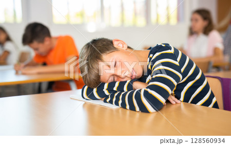 Boy is tired and sleeping at the desk in classroom Boy is tired and sleeping at the desk in classroom 128560934