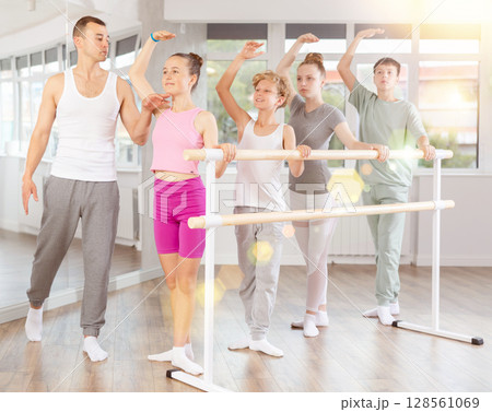 Teenage boys and girls practicing third position of ballet in dancehall Teenage boys and girls practicing third position of ballet in dancehall 128561069