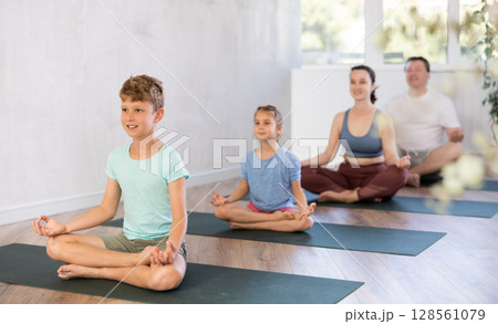 Calm preteen boy practicing lotus pose of yoga with his family 128561079