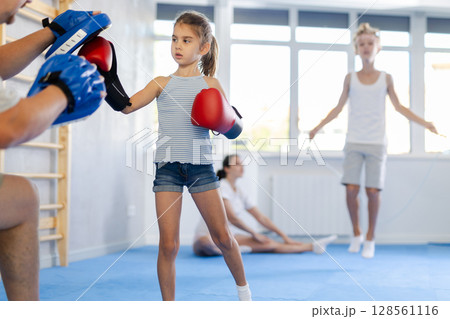 Tween girl in boxing gloves practicing punches on focus mitts in hands of father 128561116