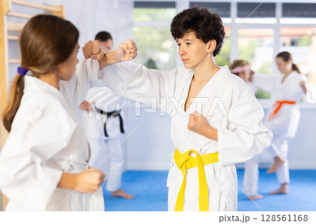 Teenagers girl and boy in kimono sparring together in gym during karate training Teenagers girl and boy in kimono sparring together in gym during karate training 128561168