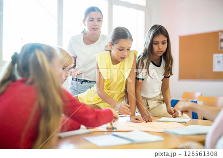 Children and teacher playing together educational board game in class Children and teacher playing together educational board game in class 128561308