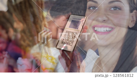 Woman holding a smartphone with qr code on screen against caucasian woman drinking a smoothie Woman holding a smartphone with qr code on screen against caucasian woman drinking a smoothie 128561812