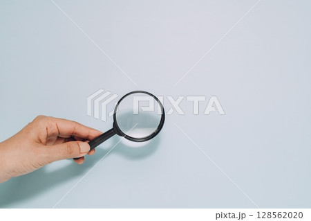 Hand Holding Magnifying Glass on Blue Background, Search and Scrutiny 128562020
