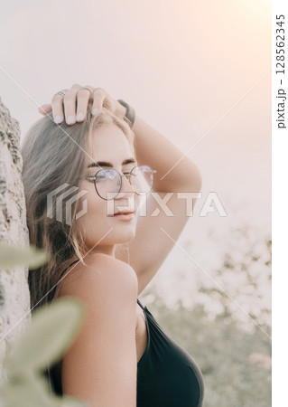Woman Glasses Beach Portrait - Woman in glasses standing by a tree on the beach looking away from the camera. Woman Glasses Beach Portrait - Woman in glasses standing by a tree on the beach looking away from the camera. 128562345