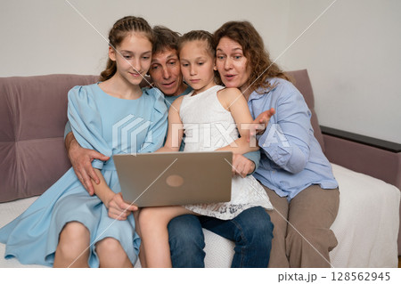 Family Laptop Togetherness: Indoors, family uses laptop for browsing, bonding on sofa during daytime. Family Laptop Togetherness: Indoors, family uses laptop for browsing, bonding on sofa during daytime. 128562945