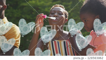 Animatin of heart balloons over happy african american family making soap bubbles in garden Animatin of heart balloons over happy african american family making soap bubbles in garden 128563862