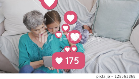 Image of heart icons and number over caucasian grandmother and granddaughter using tablet 128563869