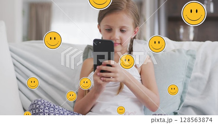 Image of smiley faces over happy caucasian girl using smartphone at home Image of smiley faces over happy caucasian girl using smartphone at home 128563874