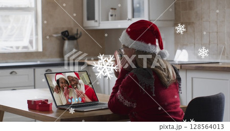 Image of snow falling over happy caucasian woman in santa hat on laptop image call 128564013