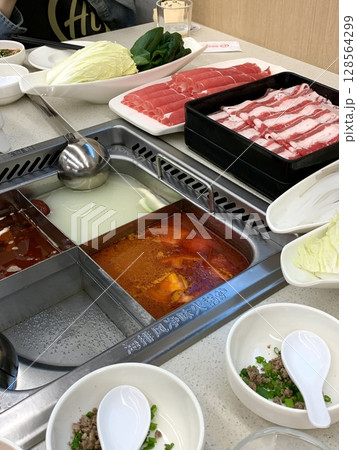 A bubbling hotpot with rich broth, tender meats, fresh vegetables, and noodles simmered to perfection. Ideal for a communal meal bursting with bold, hearty flavors. 128564299