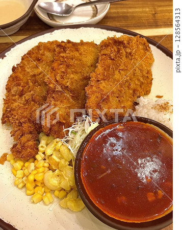 Crispy tonkatsu, a Japanese-style breaded and deep-fried pork cutlet, served with shredded cabbage and drizzled with savory sauce. A delightful balance of crunchy texture and juicy meat. 128564313