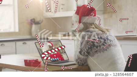 Image of candy canes falling over caucasian woman in santa hat on laptop image call at christmas Image of candy canes falling over caucasian woman in santa hat on laptop image call at christmas 128564607