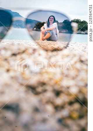Smiling woman on beach viewed through sunglasses on sand, creative vacation summer concept 128564781