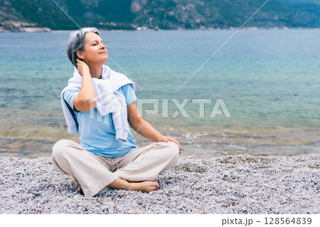 Mature Woman Enjoying Relaxation on Pebble Beach by Sea, Embracing Tranquility and Nature 128564839