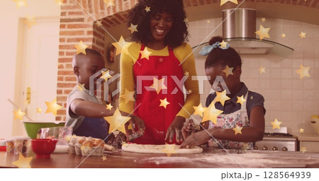Image of stars falling over happy african american mother with children baking at christmas 128564939