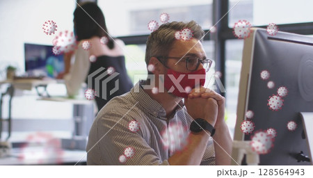 Image of covid 19 cells floating over man in face mask using computer in office 128564943