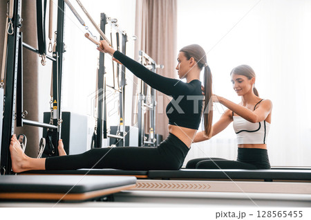 With the help of personal trainer. Women in fitness center are doing exercises 128565455