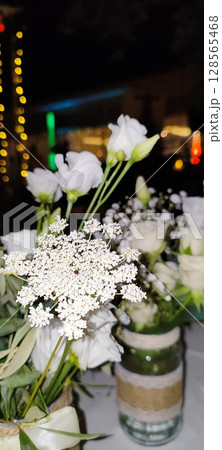 Rustic floral arrangement in jars. Festive decoration, white roses and plant branches in decorative jars. Rustic floral arrangement in jars. Festive decoration, white roses and plant branches in decorative jars. 128565468