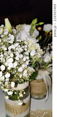 Rustic floral arrangement in jars. Festive decoration, white roses and plant branches in decorative jars. Rustic floral arrangement in jars. Festive decoration, white roses and plant branches in decorative jars. 128565469